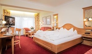 A hotel room with a wooden bed, a desk with a television, a chair, and a small table with a bottle of champagne. - Wellness Privathotel Post AN DER Therme (Badenweiler)