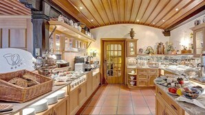 A spacious kitchen with wooden cabinets, a tiled floor, and various kitchen appliances and utensils. - Wellness Privathotel Post AN DER Therme (Badenweiler)