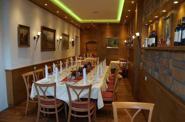 Una larga mesa de comedor preparada para una comida en un cuarto con luz cálida, paredes de madera y detalles de piedra.