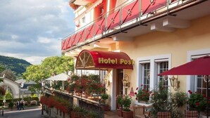 A hotel with a red awning, outdoor seating, and potted plants. - Wellness Privathotel Post AN DER Therme (Badenweiler)