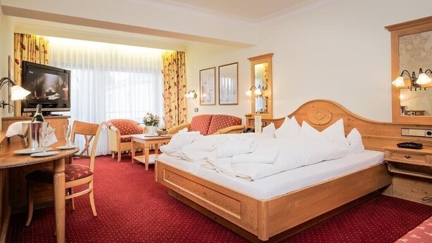 A hotel room with a wooden bed, a desk with a chair, a television, and a dining table. - Wellness Privathotel Post AN DER Therme (Badenweiler)