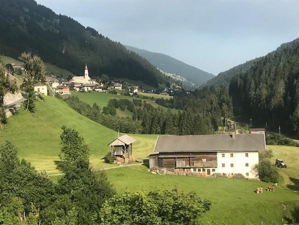 A rural landscape with a prominent white building, a small wooden structure, and a church on a hill.