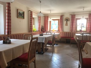 A dining area with multiple tables and benches, a painting on the wall, and a window with curtains.