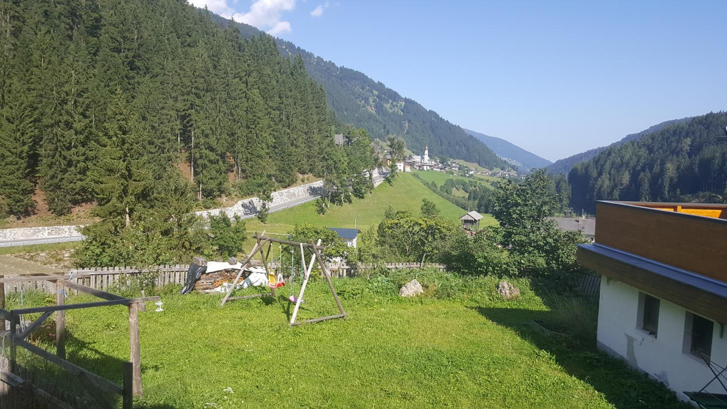 Paisaje rural con una zona cubierta de hierba, una cerca de madera y un edificio con techo inclinado.