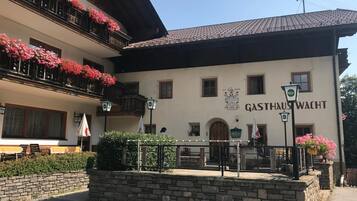 Ein Gebäude mit einem Schild, auf dem 'GASTHAUS WACHT' steht, und einer Steinmauer im Vordergrund.