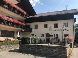 A building with a sign reading 'GASTHAUS WACHT' and a stone wall in front.