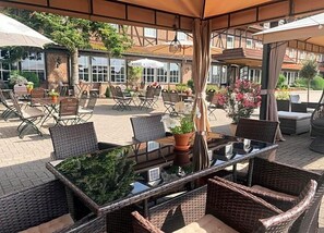 An outdoor patio area with tables and chairs, surrounded by brick walls and potted plants.