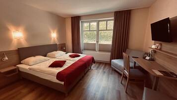 Ein Hotelzimmer mit Bett, Nachttischen, Schreibtisch, Stuhl, Fernseher und einem fenster mit Vorhängen.