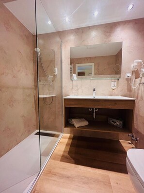 A modern bathroom with a glass shower enclosure, a wooden vanity, and a large mirror.