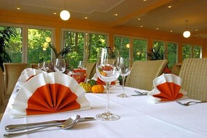 A dining table set with white tablecloths, orange napkins, and clear wine glasses.