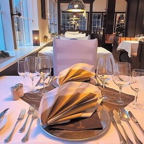 A dining table set with a folded napkin, wine glasses, cutlery, and a candle.