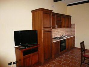 A compact kitchen with wooden cabinets, a built-in stove, and a television on a stand.