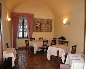 A dining area with tables set for four, a large painting on the wall, and a window with curtains.