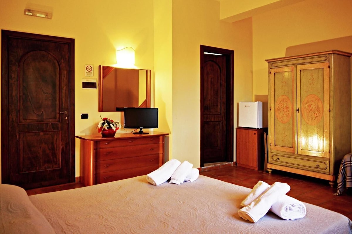 A hotel room with a bed, a desk with a computer, a wardrobe, and a door.