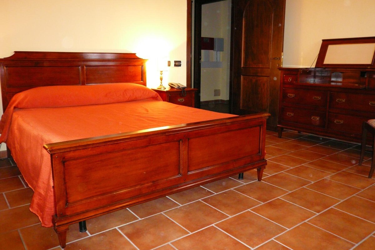 A bedroom with a wooden bed, a nightstand, a dresser, and a door leading to another room.