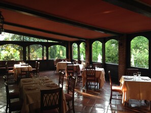 A restaurant with multiple tables and chairs, large windows, and a view of greenery outside.