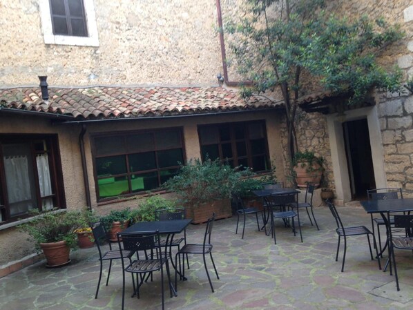 A courtyard with a tiled roof, stone walls, and potted plants. There are outdoor tables and chairs arranged for dining.