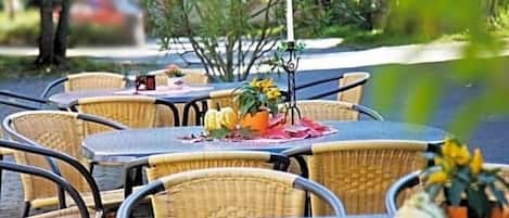 Outdoor tables with wicker chairs, some with flowers and candles, set in a garden area.
