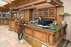 A wooden reception desk with a green marble top, surrounded by wooden cabinets and a large window. - Hotel Krone (Nellingen)