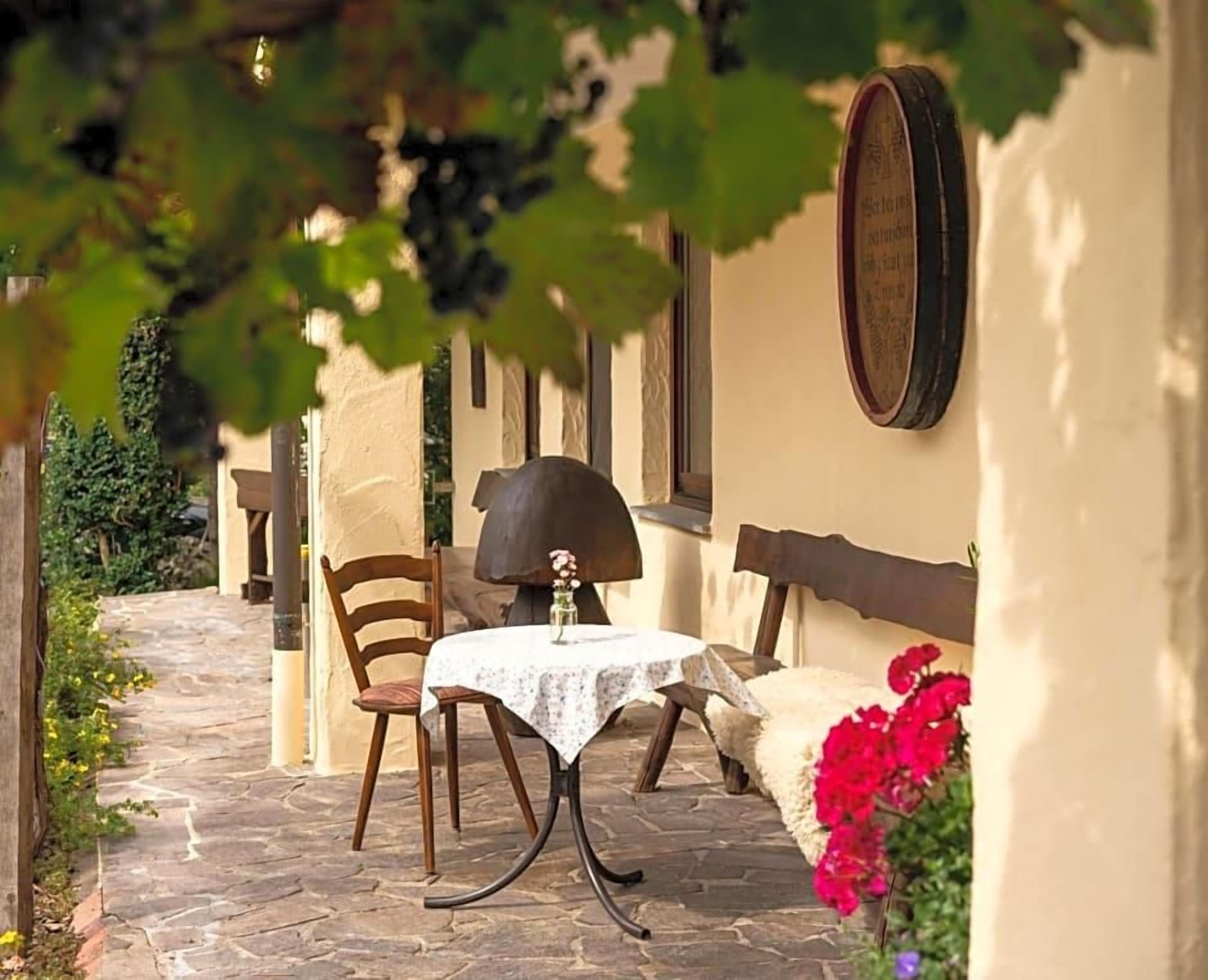 A stone-paved outdoor area with a table and chairs, a bench, and a wall-mounted plaque.