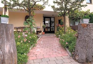 A paved pathway leading to a building entrance, surrounded by lush greenery and flowering plants. - Hotel Krone (Nellingen)