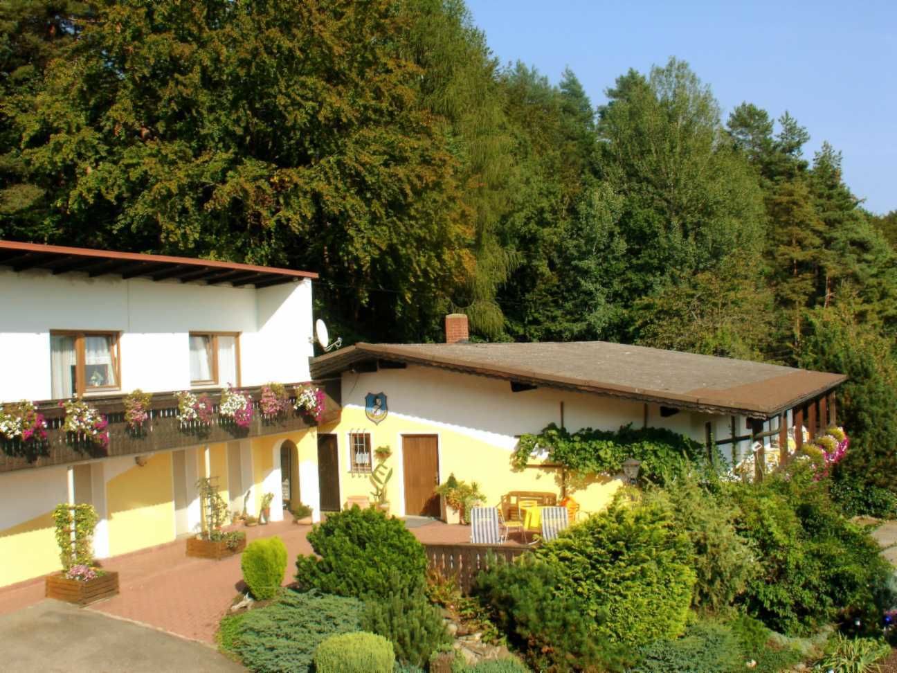 A two-story building with a balcony, a wooden deck, and a garden area with potted plants and flowers.