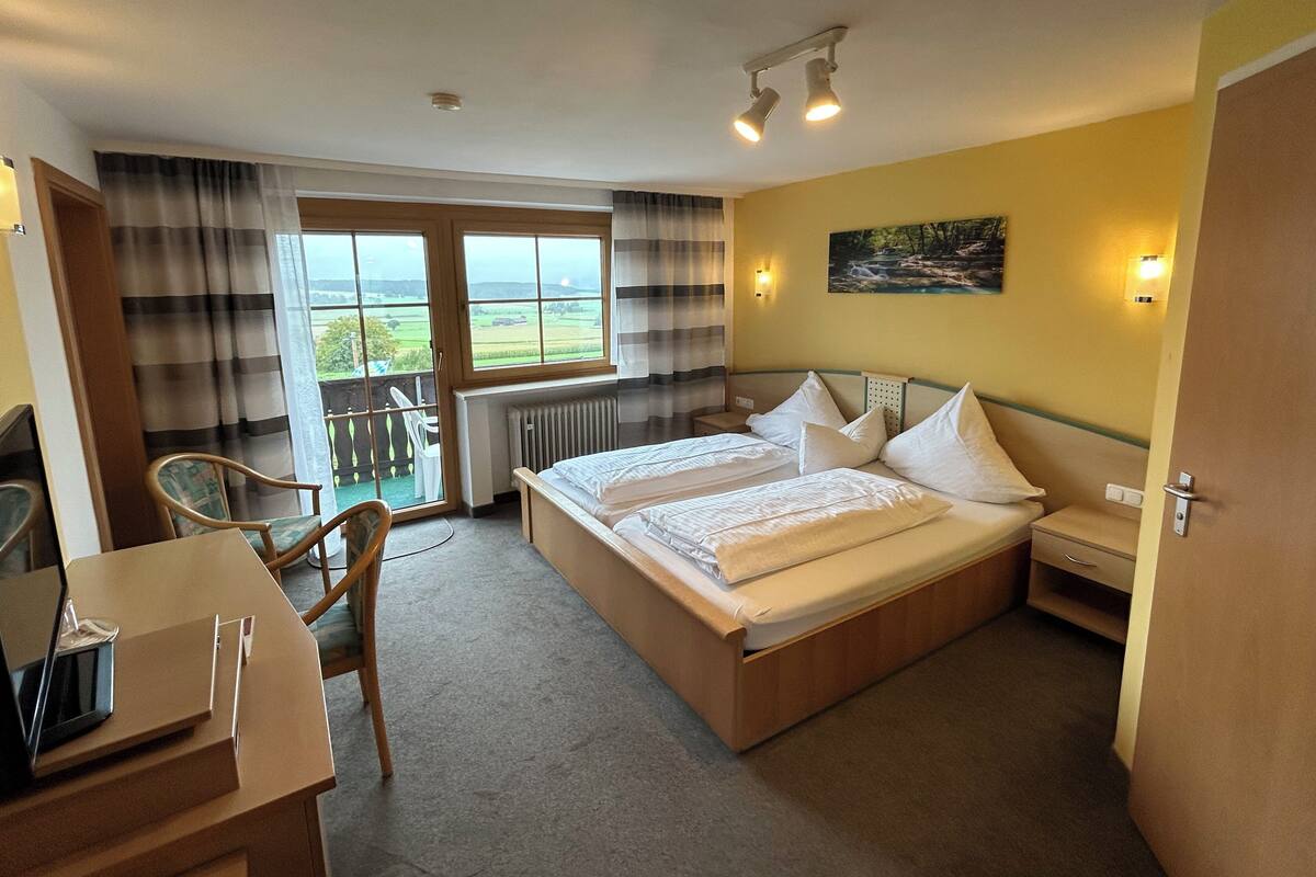 A bedroom with a bed, a desk, a chair, a window with curtains, and a painting on the wall.