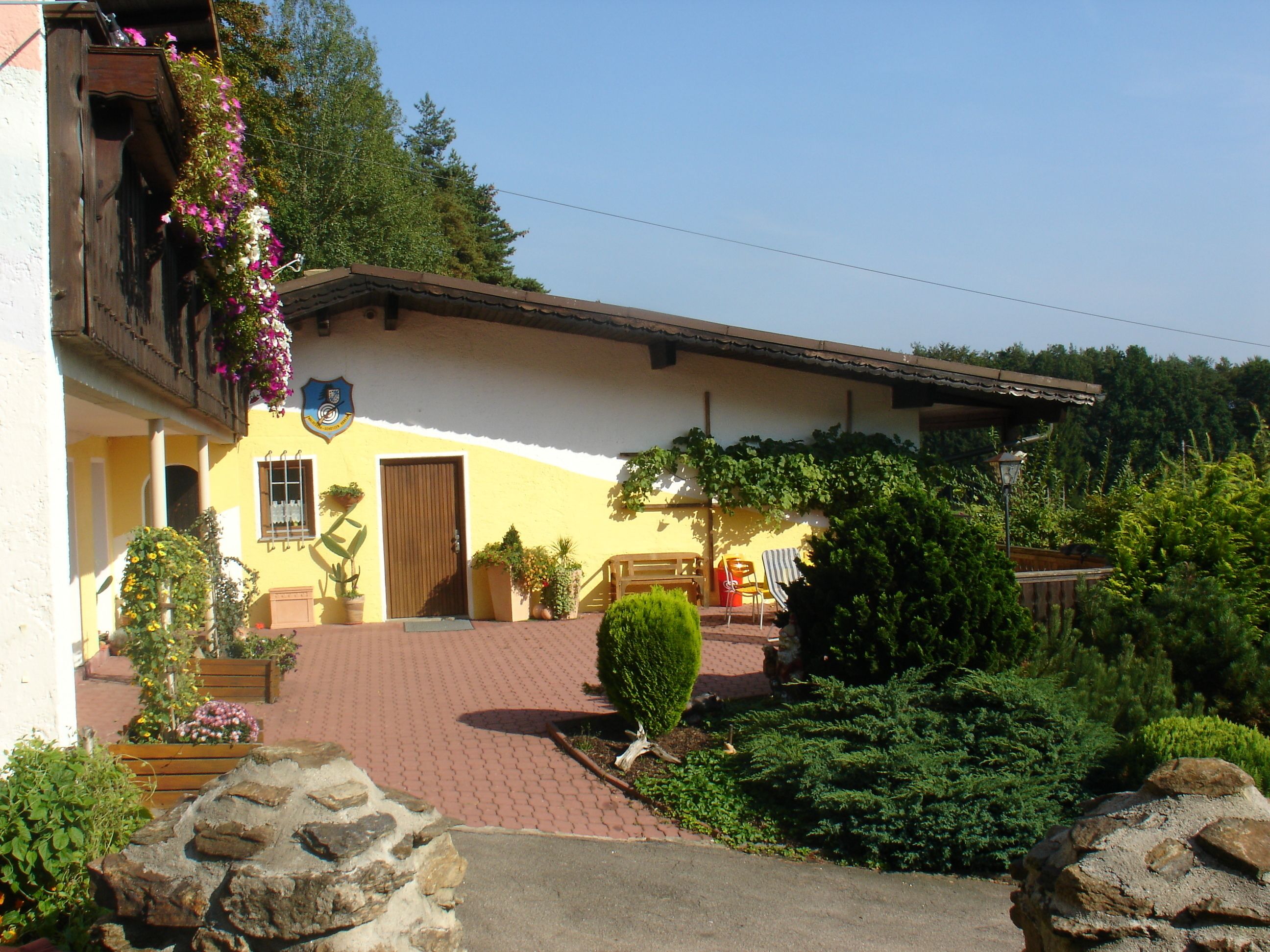 A yellow building with a wooden door, potted plants, and a bench outside.