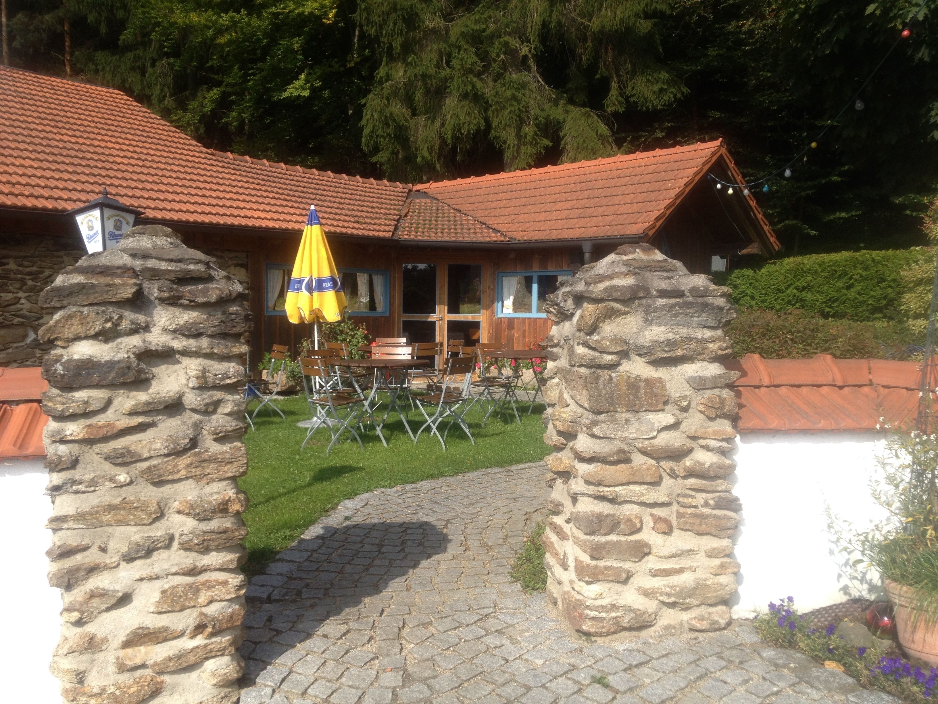 Un arc en pierre mène à un chalet en bois doté d’un toit en tuiles, d’un espace salon extérieur et d’un parasol jaune.