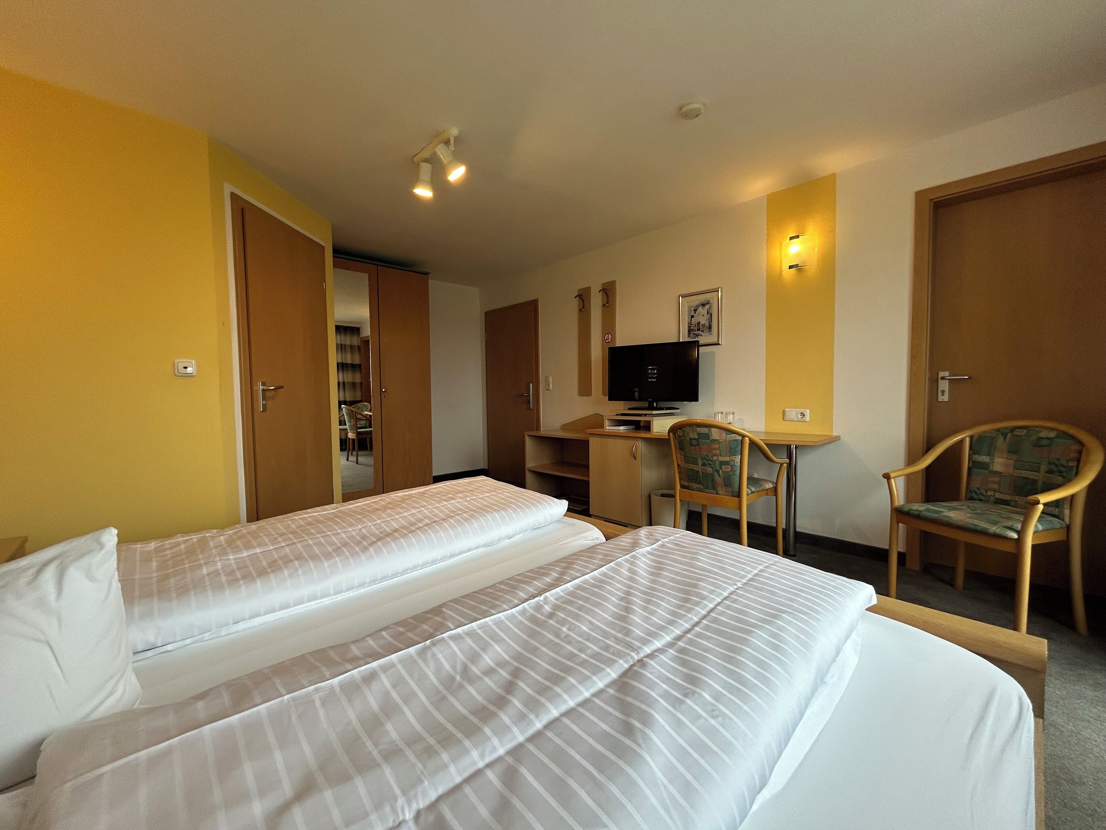 A hotel room with two beds, a desk with a computer, a chair, and a television.
