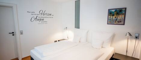 Une chambre à coucher avec un lit, des lampes de chevet, une citation sur le mur, une porte et un tableau.