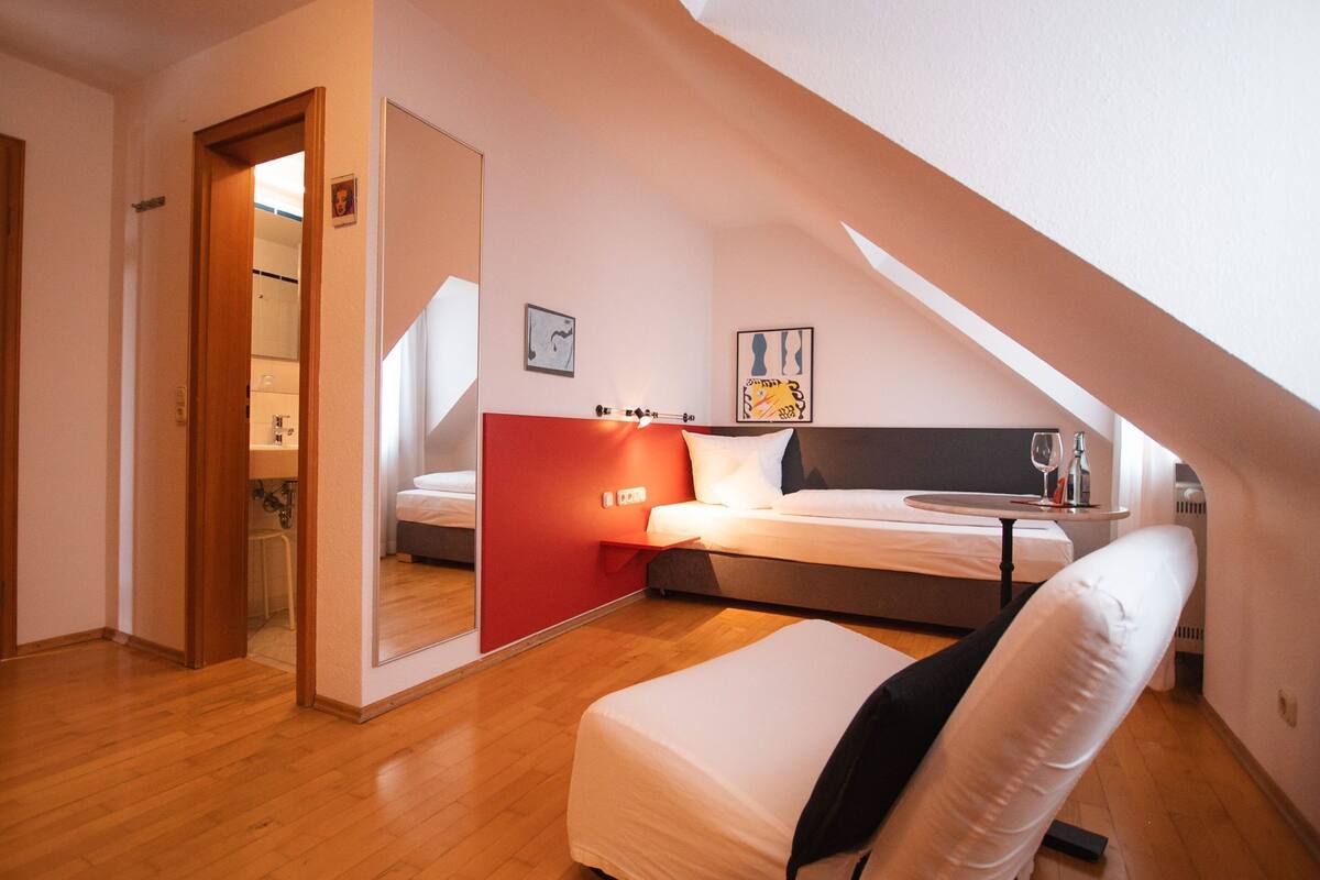 A bedroom with a bed, a bedside table, a chair, and a small table with a glass and bottle.