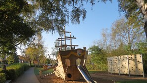 Une aire de jeux avec une structure ludique en forme de navire de pirate, comprenant un toboggan et un filet d’escalade.