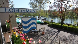 Une enseigne d’hôtel avec un motif représentant une vague, des tables à l’extérieur sous des parasols et une vue sur un lac.
