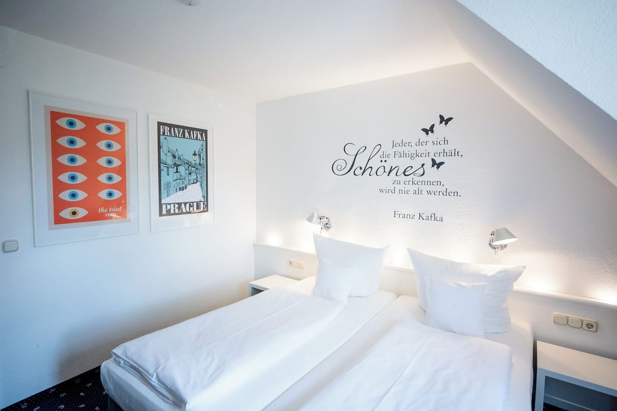 A hotel room with a neatly made bed, a wall with framed artwork, and a motivational quote.