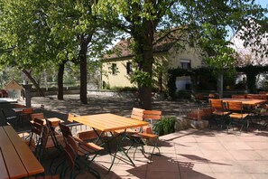 An outdoor seating area with wooden tables and chairs, surrounded by trees and a building in the background. - Hotel am Main (Veitshoechheim)