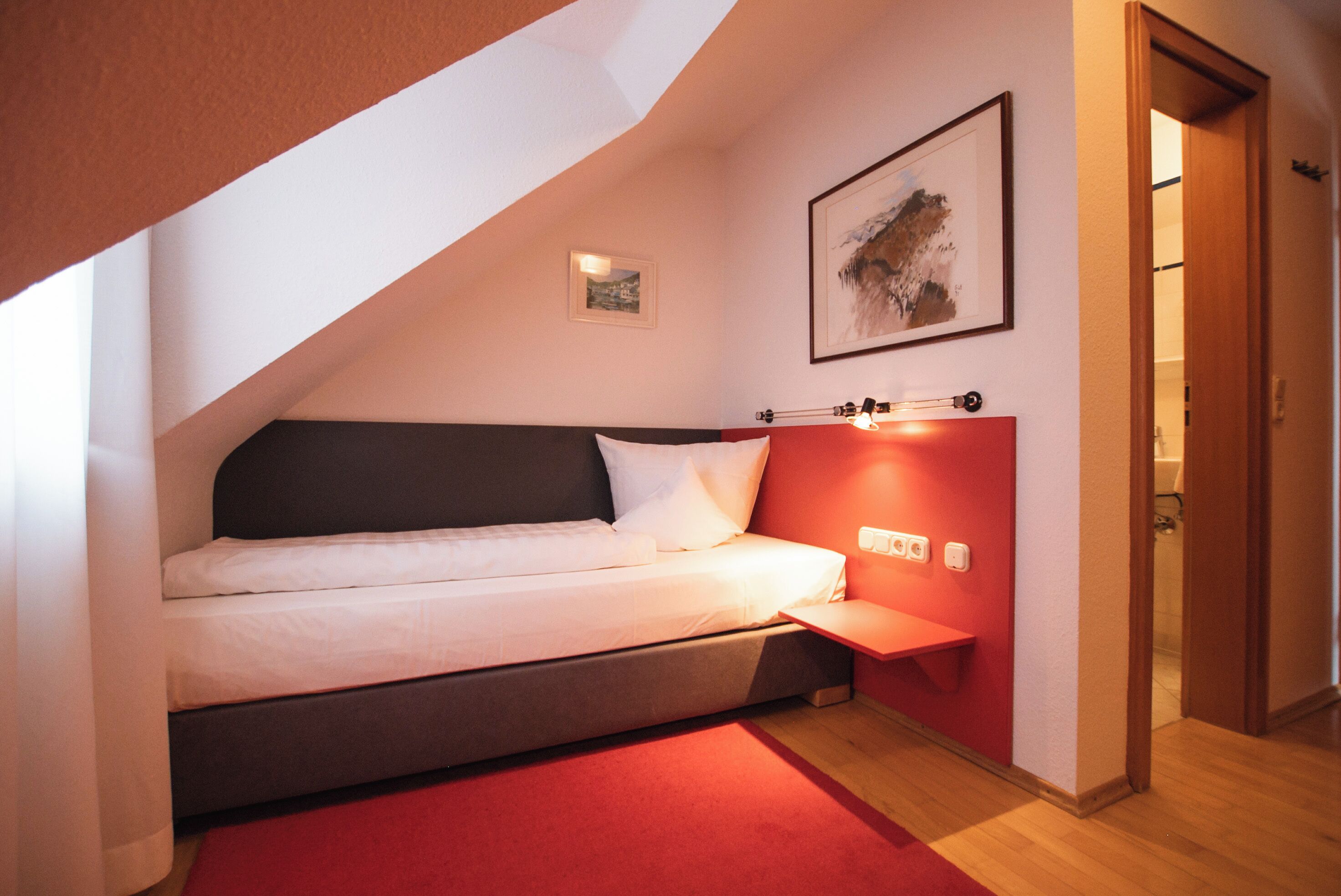 Une chambre à coucher avec un lit, un mur d’accent de couleur rouge, une petite table de chevet et un tableau encadré accroché au mur.