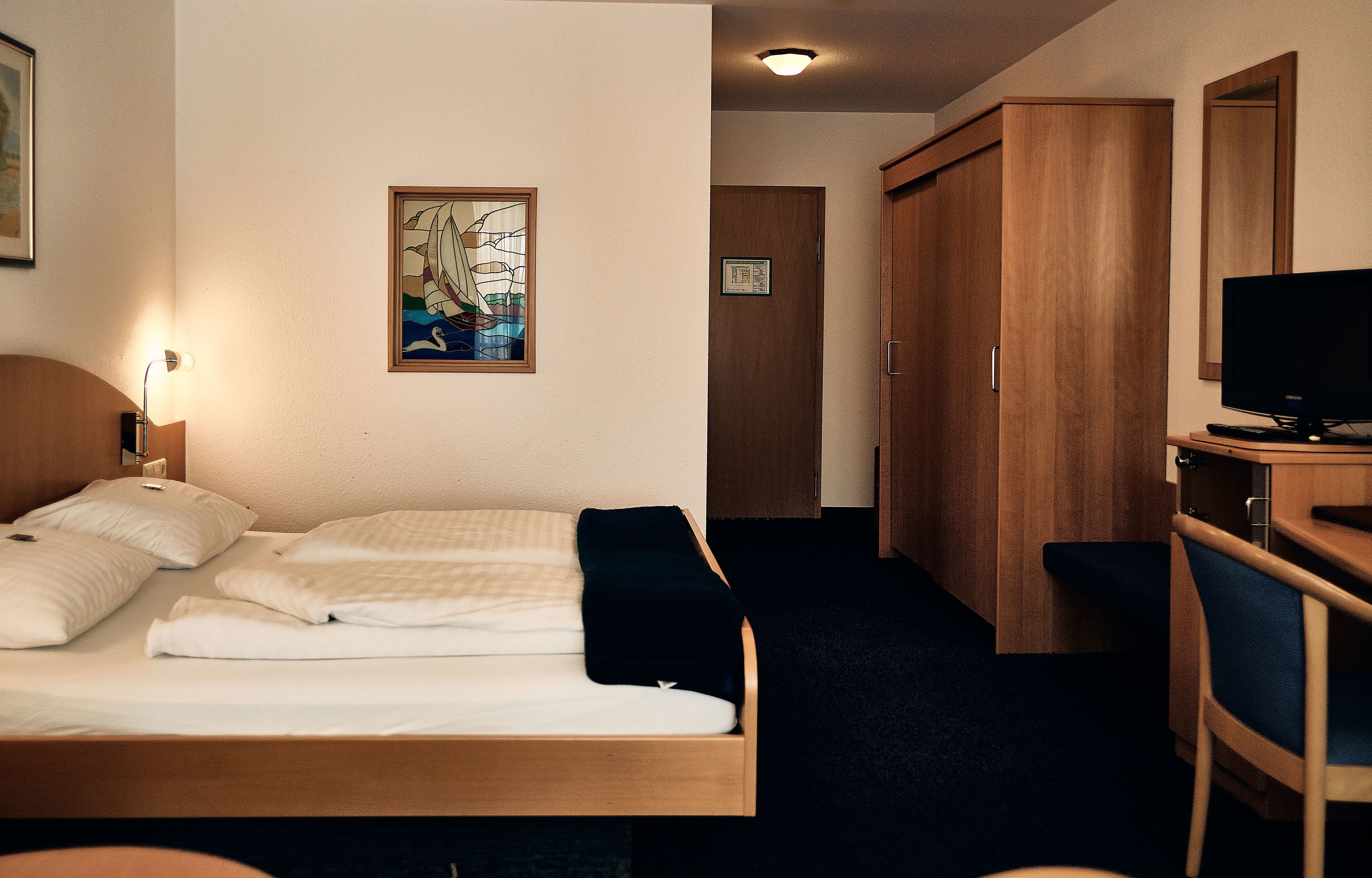 Una camera d'albergo con un letto, una scrivania con un computer, una televisione e un armadio.