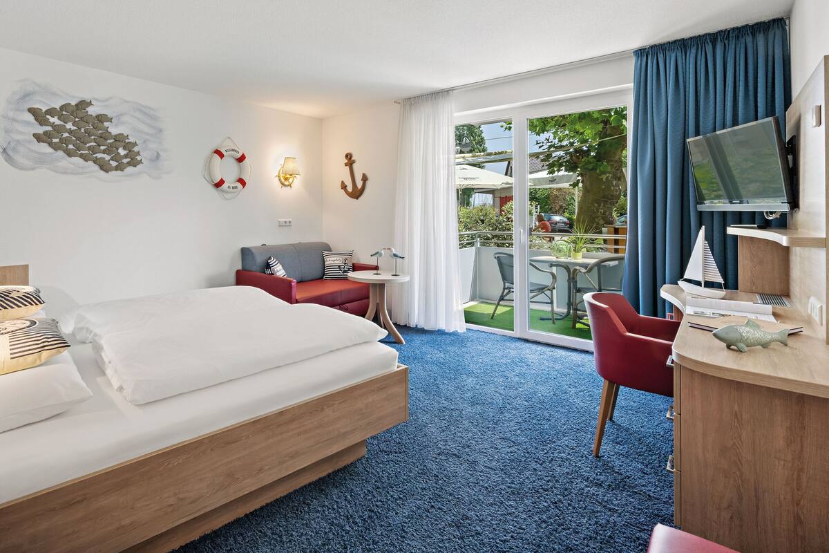 A hotel room with a bed, a desk, a chair, a TV, and a balcony with a table and chairs.