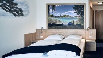 Una habitación de hotel con una cama, un cuadro de una playa y un cabecero de madera.