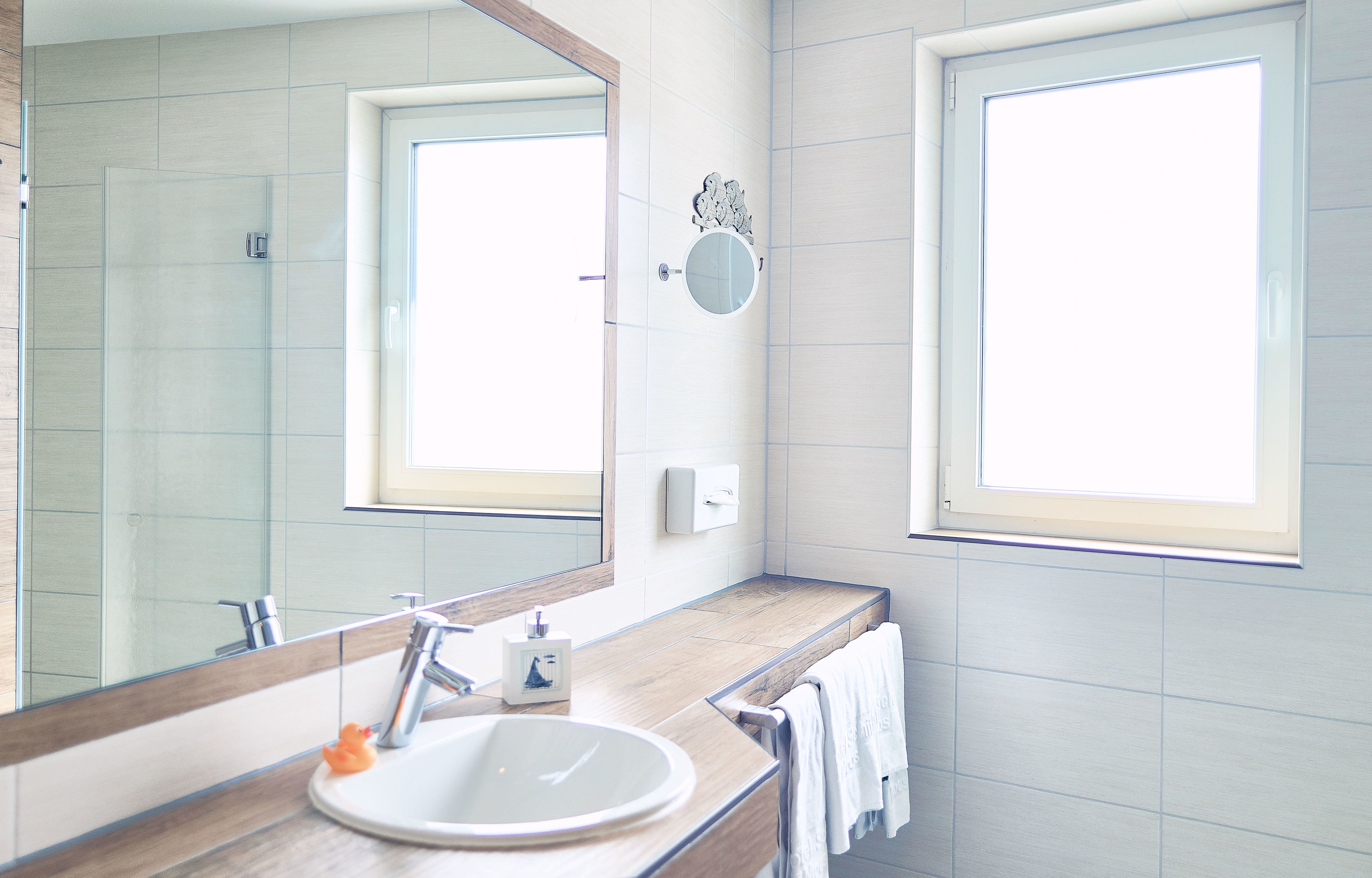 A bathroom with a large mirror, a sink, a towel rack, and a window.
