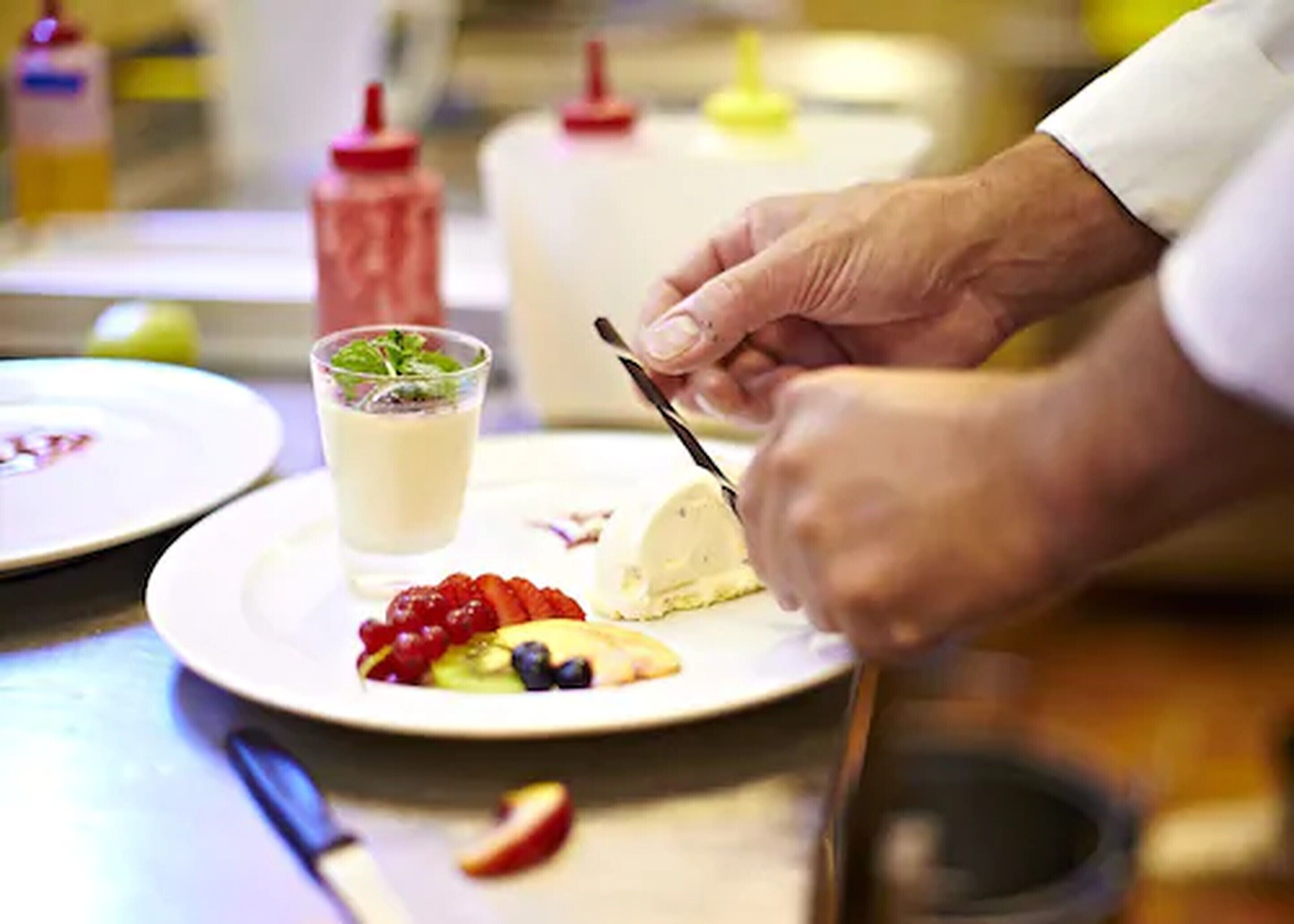 Una persona cortando un postre en un plato con frutas y una bebida.