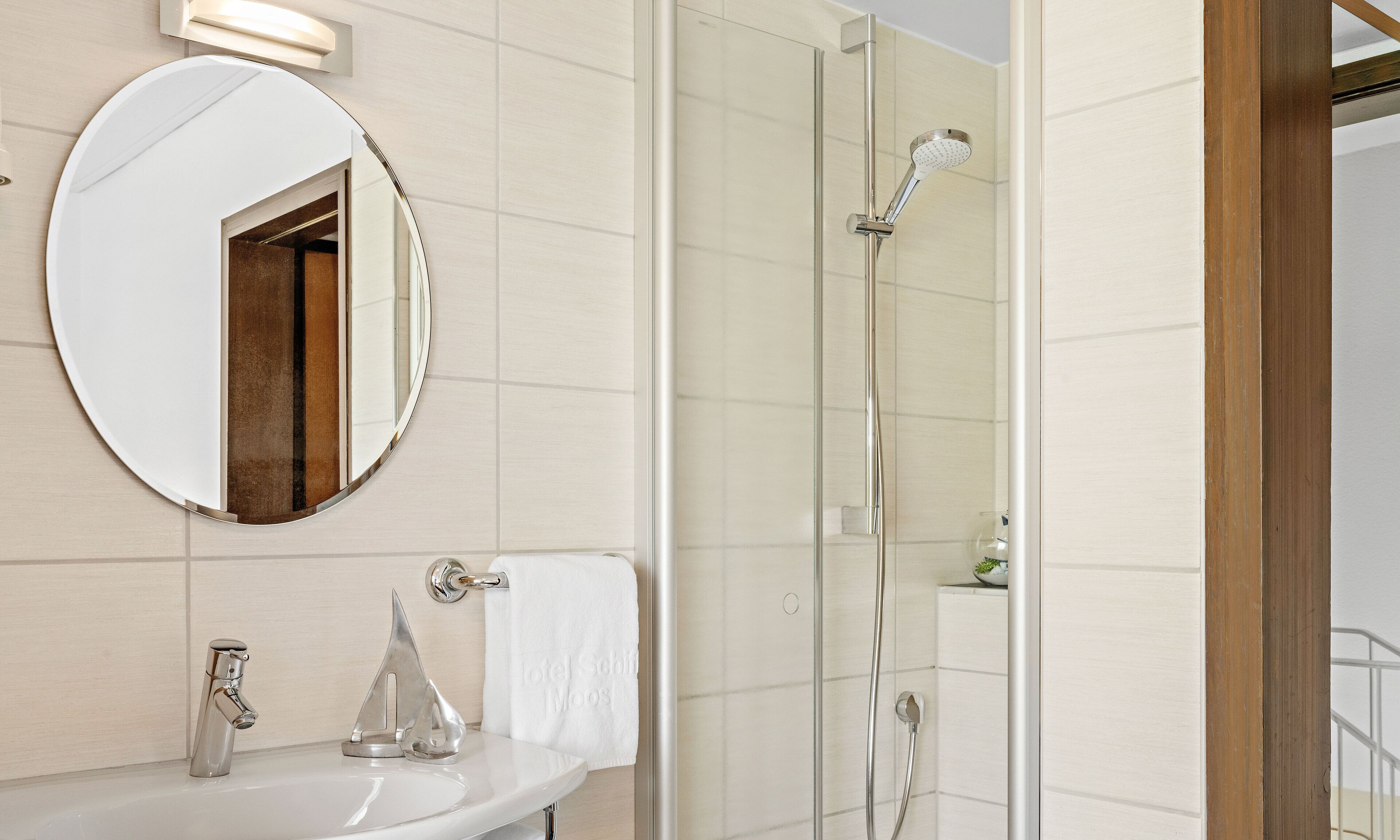 A bathroom with a round mirror, a sink, a shower with a handheld showerhead, and a towel rack.