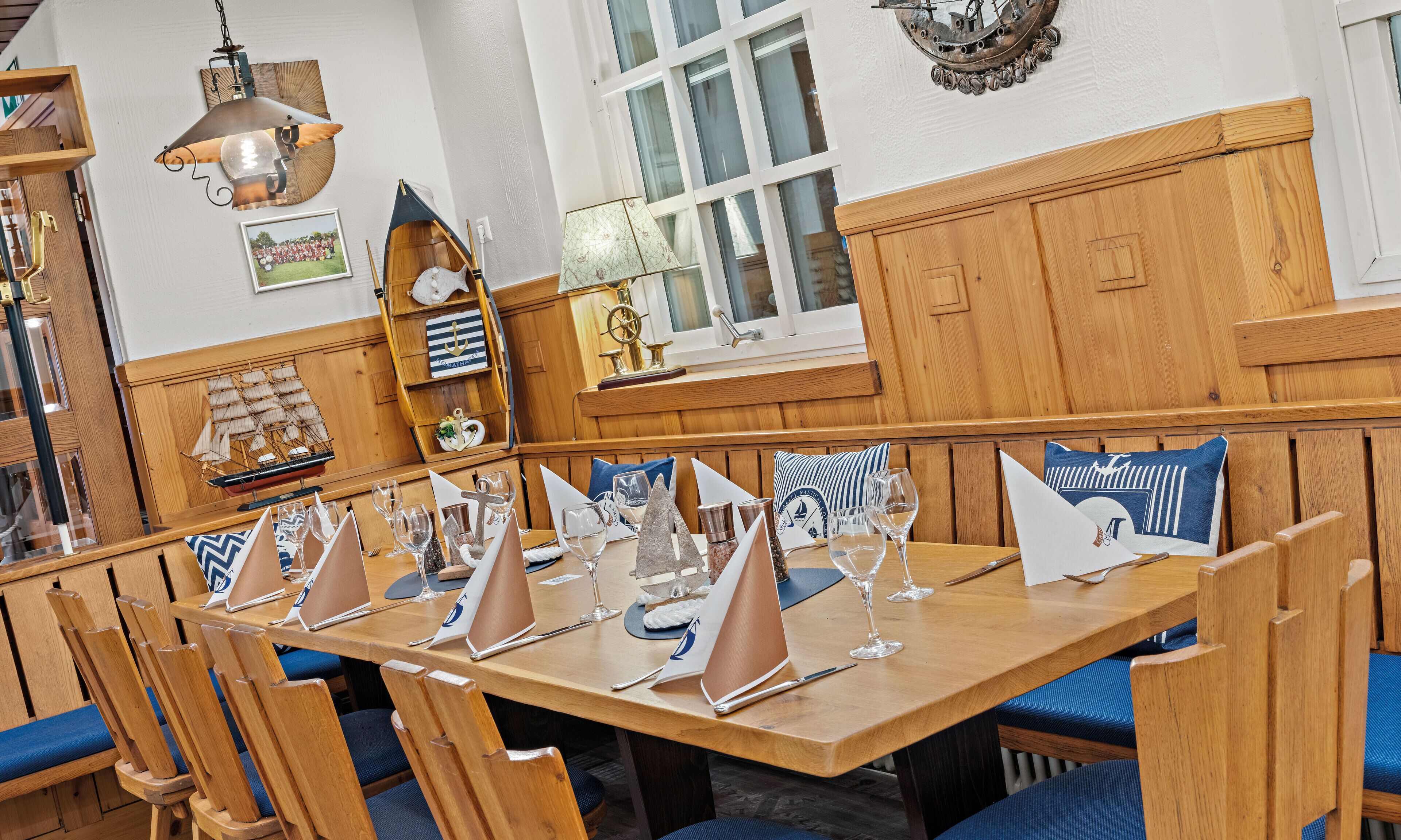 Una mesa de comedor de madera con sillas tapizadas en azul, dispuesta con copas de vino y servilletas.