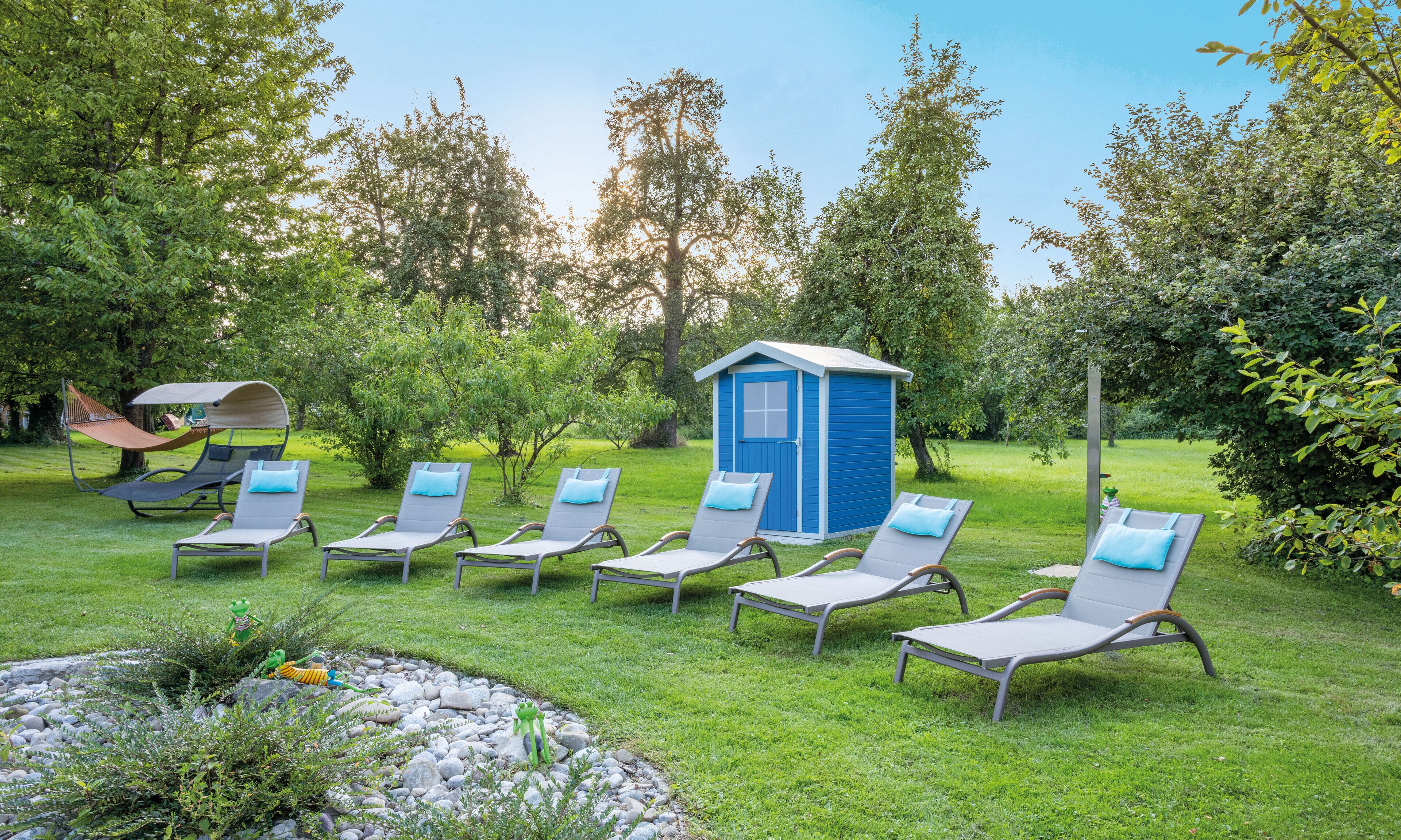 Un jardín con seis sillones de descanso y un cobertizo azul.