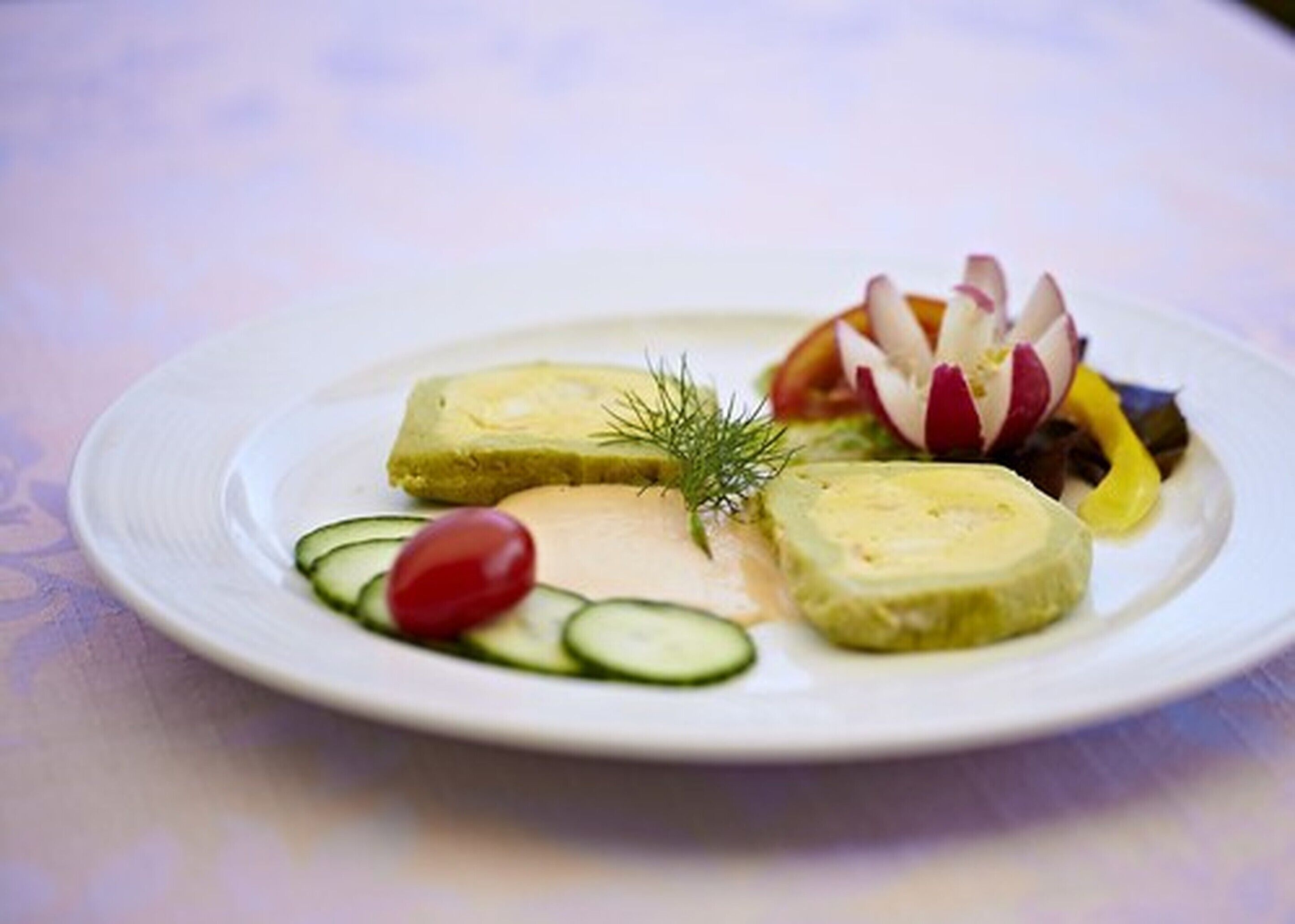 Een bord met verschillende soorten eten, waaronder plakjes komkommer, een kers tomaat en een decoratieve groentenopstelling.