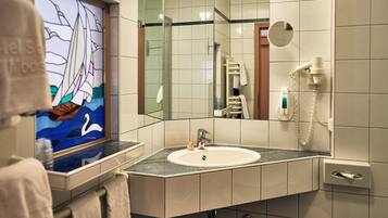 Un baño con un espejo grande, un lavabo, un perchero para toallas y una cabina de ducha con mampara de cristal.