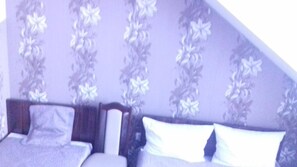 A bedroom with a sloped ceiling, a bed with white bedding, and floral wallpaper. - Prymus (Radom)