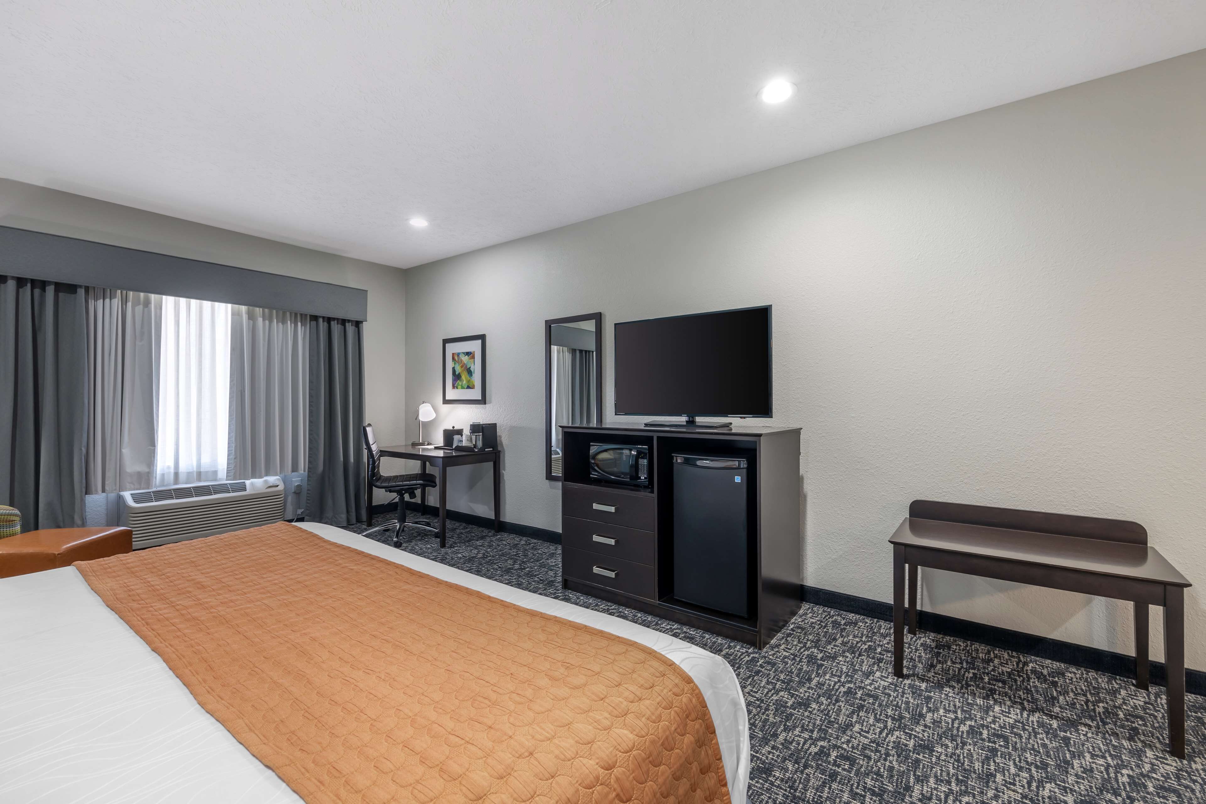 Habitación de hotel con cama, escritorio, televisor, mini refrigerador y una banca.