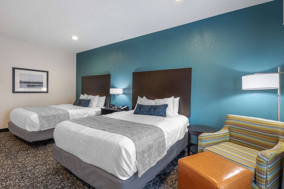Habitación de hotel con dos camas, un sofá, una silla y un cuadro en la pared.
